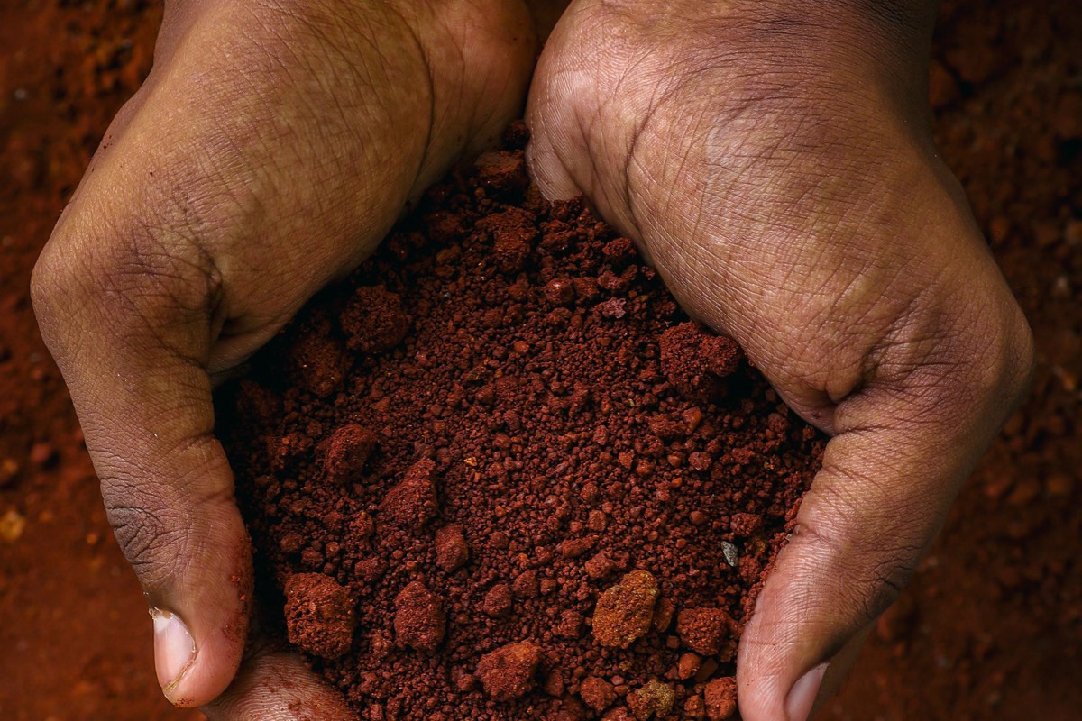 Hands holding a scoop of red clay soil.