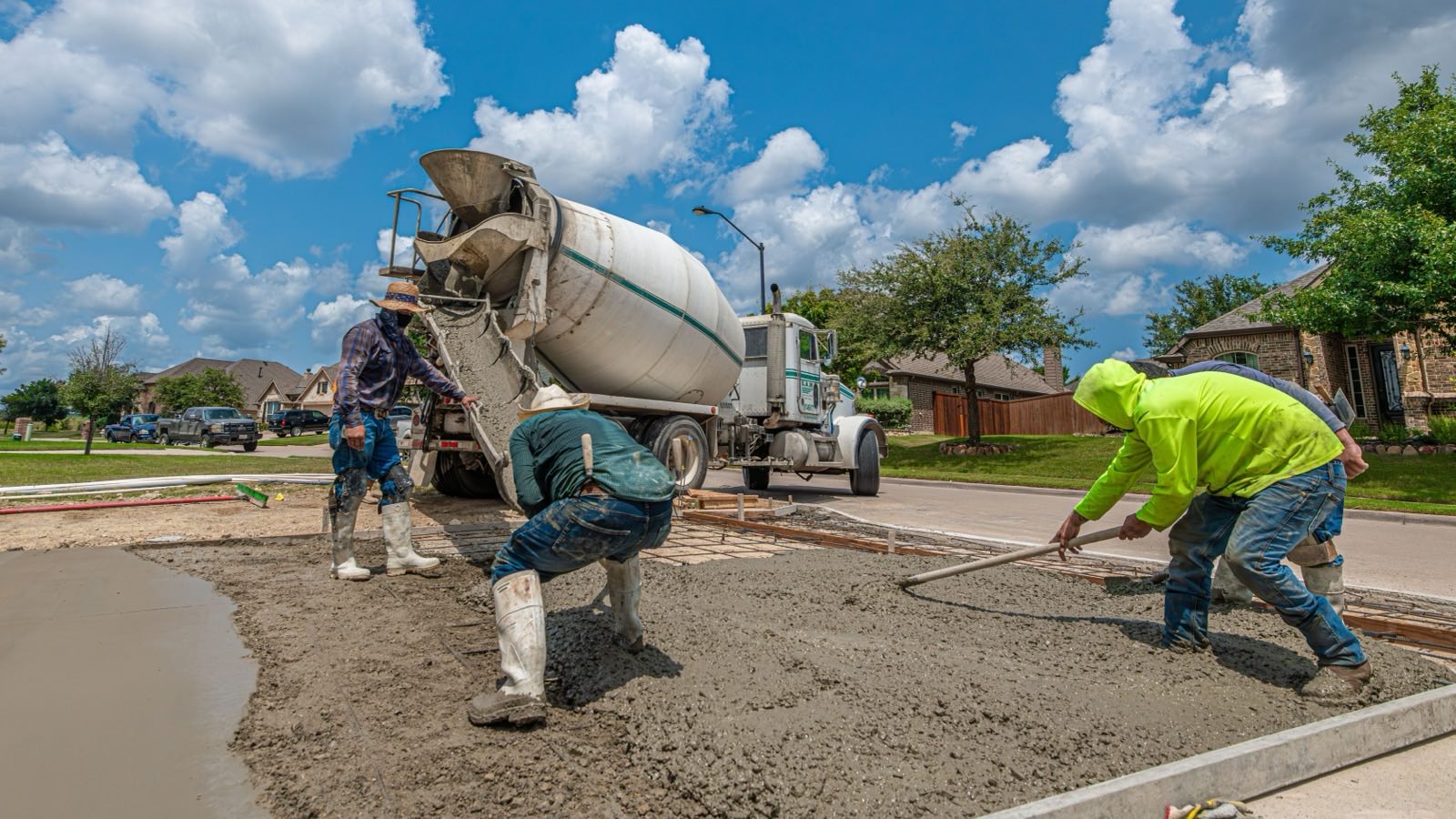 Workers spreading wet concrete behind a cement mixer truck on a building site