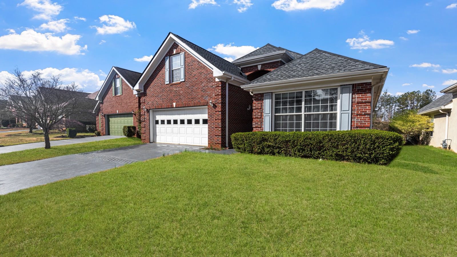 Red brick house with a two-car garage and a large green lawn under a blue sky