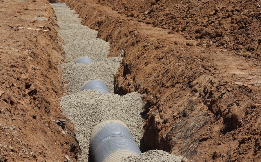 Gravel-filled trench with corrugated drain pipe laid in red clay soil