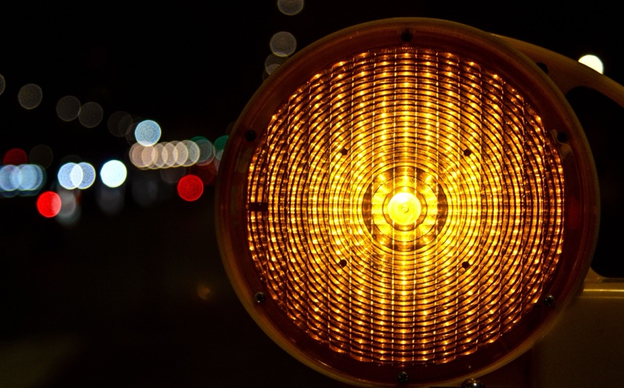 Amber warning lamp glowing at night on a dark street, with blurred lights behind it