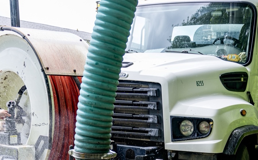 White septic pump truck cab with a green suction hose and a hose reel